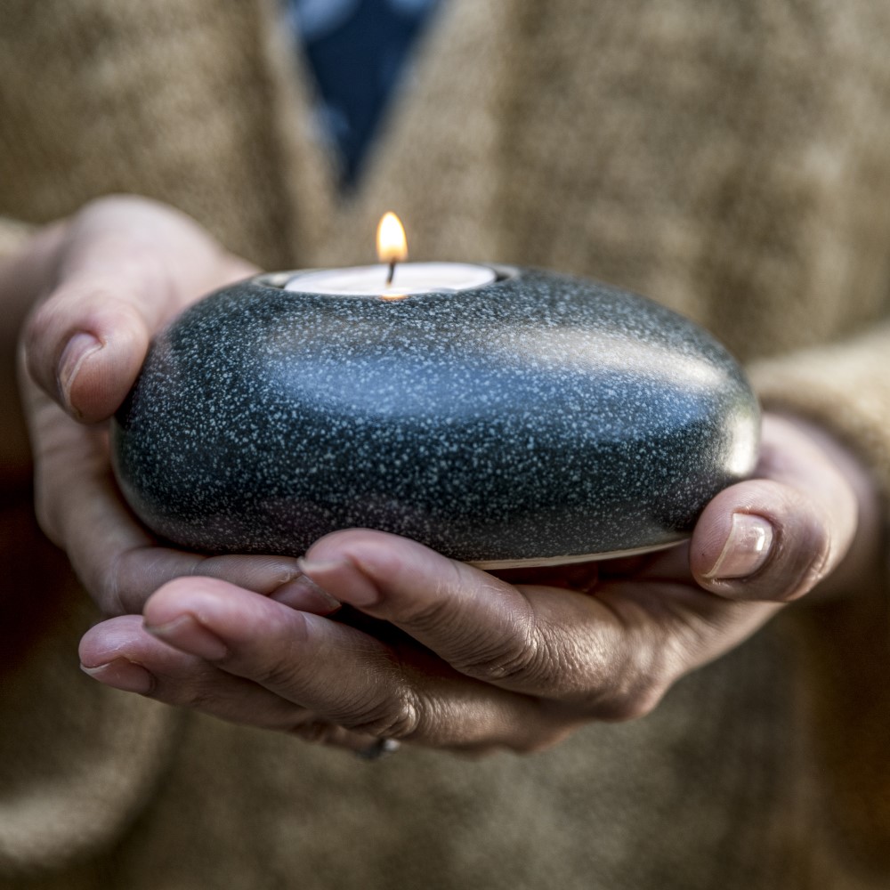 Grieving Lady holds an Eternity Pebble Keepsake Memorial Candle with lit candle of remembrance.