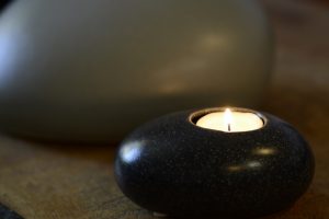 Pebble shaped Adult funeral urn on display on wooden surface with lit candle of remembrance