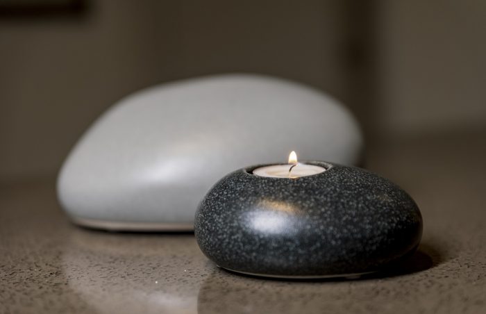 Pebble shaped Child/Infant funeral urn on display on granite surface with lit candle of remembrance