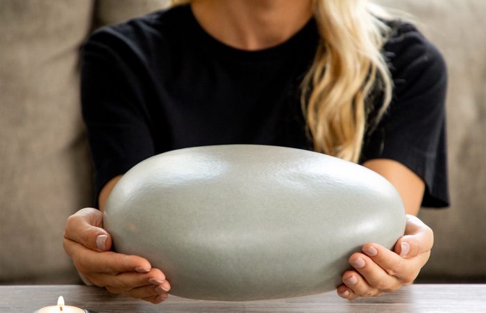Eternity Pebble Adult Funeral Urn close up with memorial candle held by grieving woman over a table