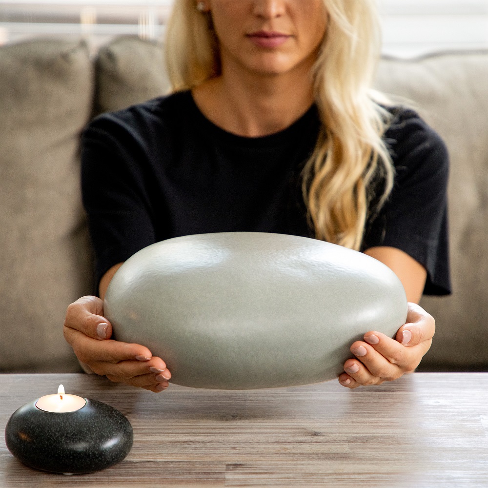 Eternity Pebble Adult Funeral Urn close up with memorial candle held by grieving woman over a table