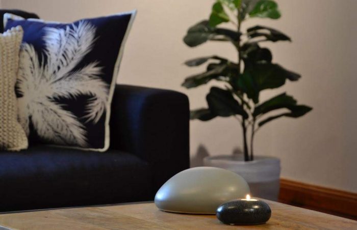 Pebble Shaped Miscarriage Funeral Urn displayed on Coffee Table paired with a Memorial Candle of Remembrance